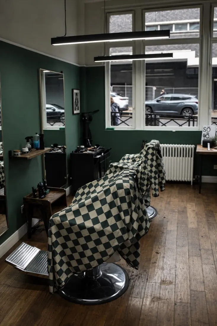 Barber chairs draped in checkerboard capes by the window